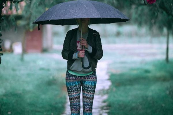 Crop woman in activewear standing under umbrella on rainy day